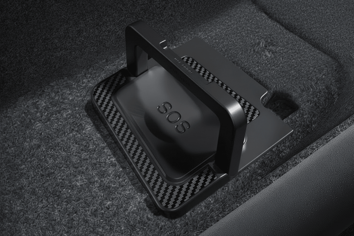 A black SOS emergency locator device with a bright orange handle, resting on a carbon-fiber-textured mat inside a dark carpeted compartment. tesla-model-y-juniper-model-3-highland-rear-door-emergency-handle-mechanical-unlock-for-switch-pull-rope-teslary-dublin-ireland-cork-nederlands-deutschland-espa-5724537_f486ca2e-ada1-4d79-8f2a-5d873537f7f3