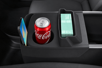 A dark gray center console organizer tray holding a paper coffee cup, a smartphone in a side pocket, and a rectangular card or case in a light green sleeve, shown inside a vehicle interior. tesla-model-y-juniper-standard-centre-console-cup-holder-with-storage-box-for-tesla-for-model-y-juniper-standard-version-only-organizer-accessories-interior-sto-5963228